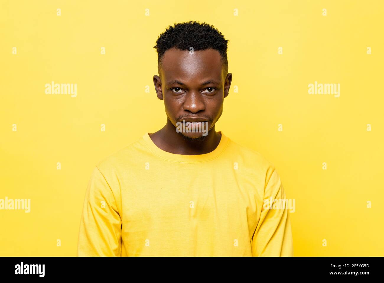 Le jeune homme africain est confronté sur fond de studio jaune isolé Banque D'Images