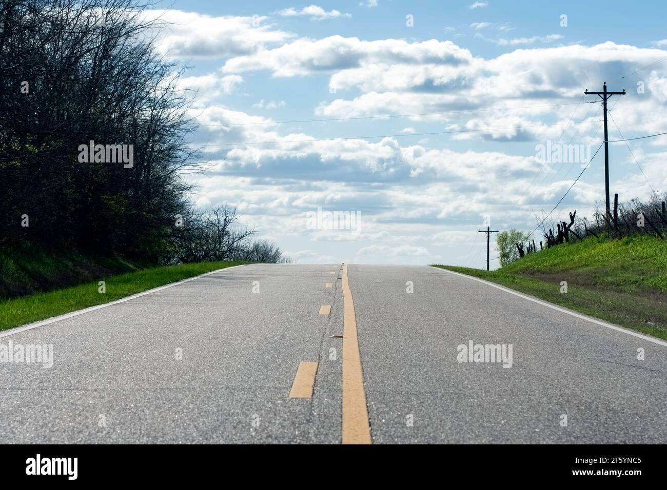 Photo d'une route rurale à deux voies qui monte une colline, apparemment dans les nuages du ciel. Banque D'Images