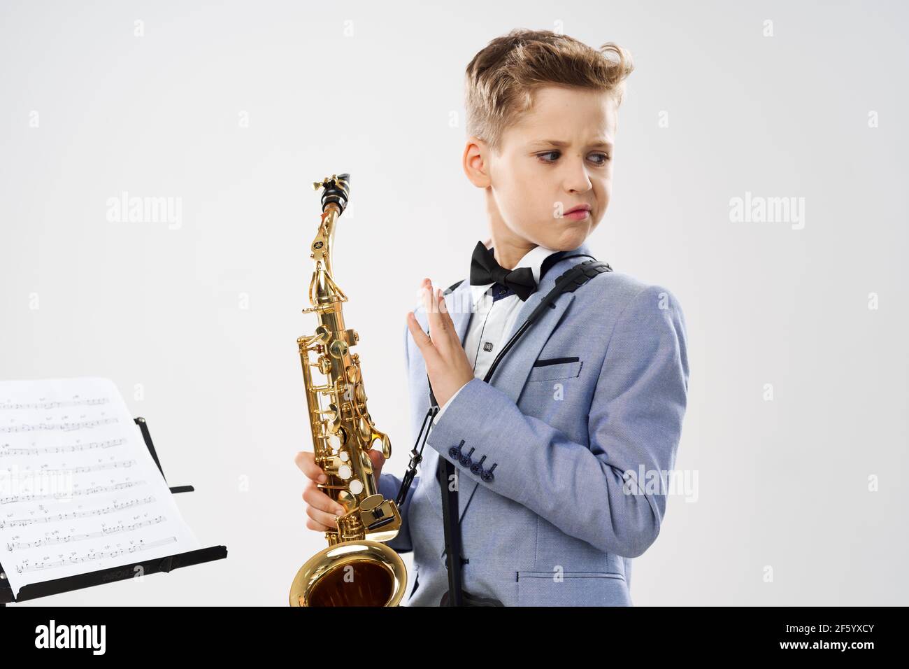 un musicien de garçon dans une combinaison classique tient un saxophone dedans sa main sur fond blanc Banque D'Images