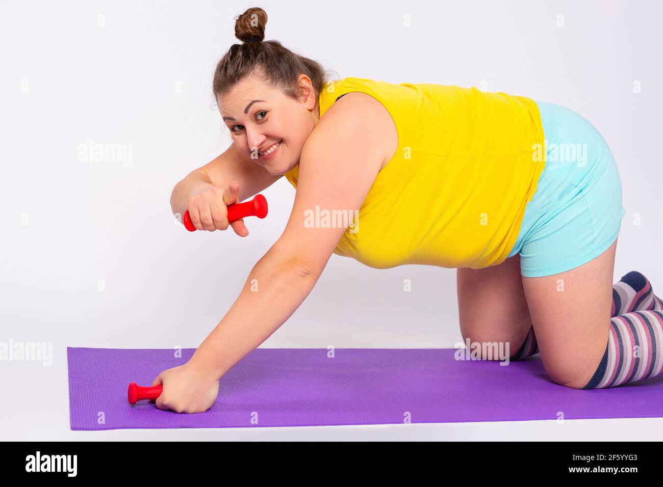 Graisse femme perte de poids exercice sur le tapis de fitness, entraînement, la bosse tenant des haltères au-dessus des triceps et des muscles biceps extension, sourire montrant Banque D'Images