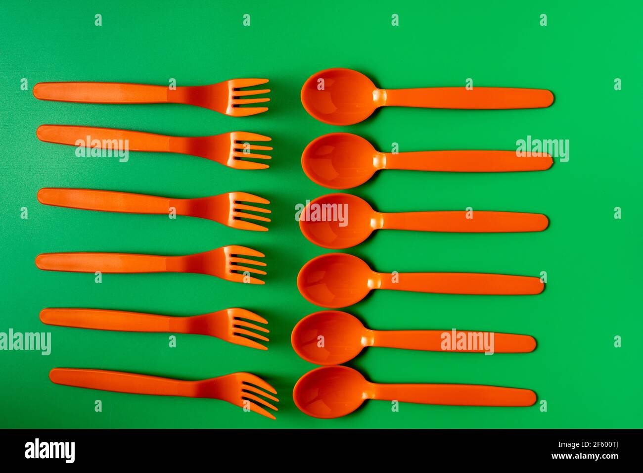 Cuillères et fourchettes en plastique orange sur fond vert. Concept écologique et sans plastique. Banque D'Images