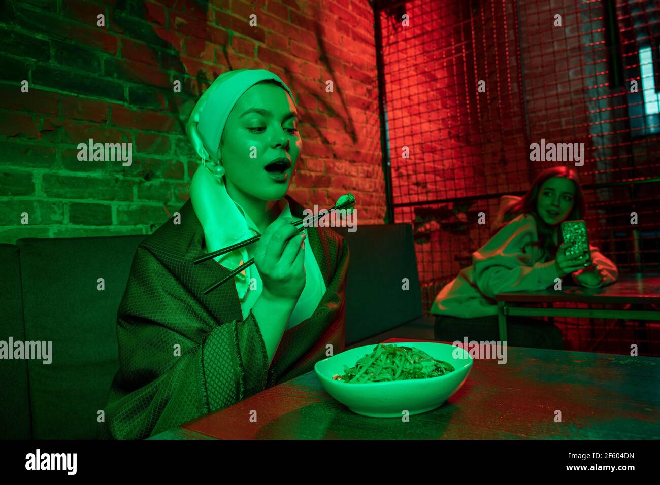 Belle fille avec une boucle d'oreille de perle prenant le déjeuner dans un café moderne, restaurant à la lumière du néon Banque D'Images