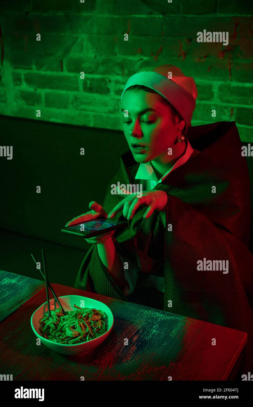 Belle fille avec une boucle d'oreille de perle prenant le déjeuner dans un café moderne, restaurant à la lumière du néon Banque D'Images