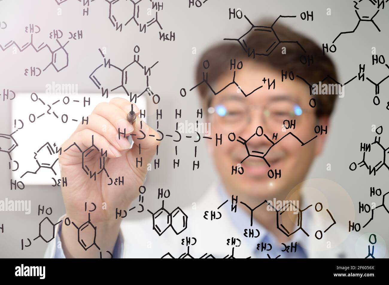 Scientifique asiatique d'âge moyen souriant et écrivant des formules chimiques sur du verre transparent. Banque D'Images