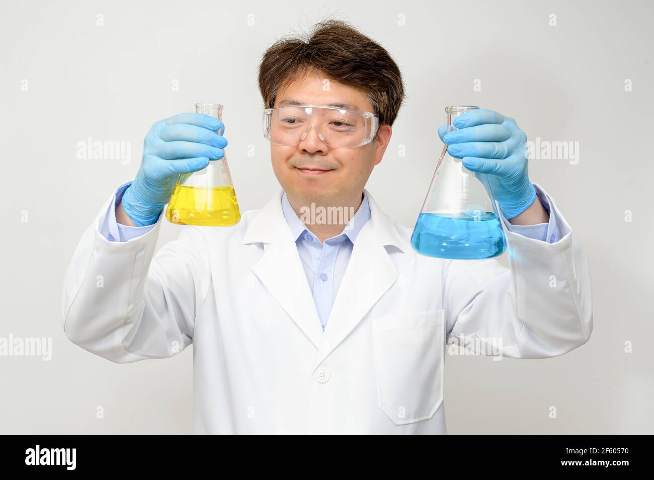 Portrait d'un scientifique asiatique de milieu d'année portant une blouse de laboratoire blanche et des gants et tenant un conteneur expérimental dans la main. Banque D'Images