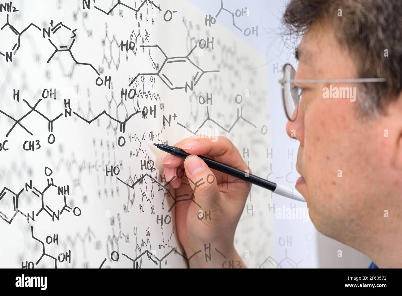 Un scientifique asiatique d'âge moyen écrit des formules chimiques sur un tableau blanc. Banque D'Images