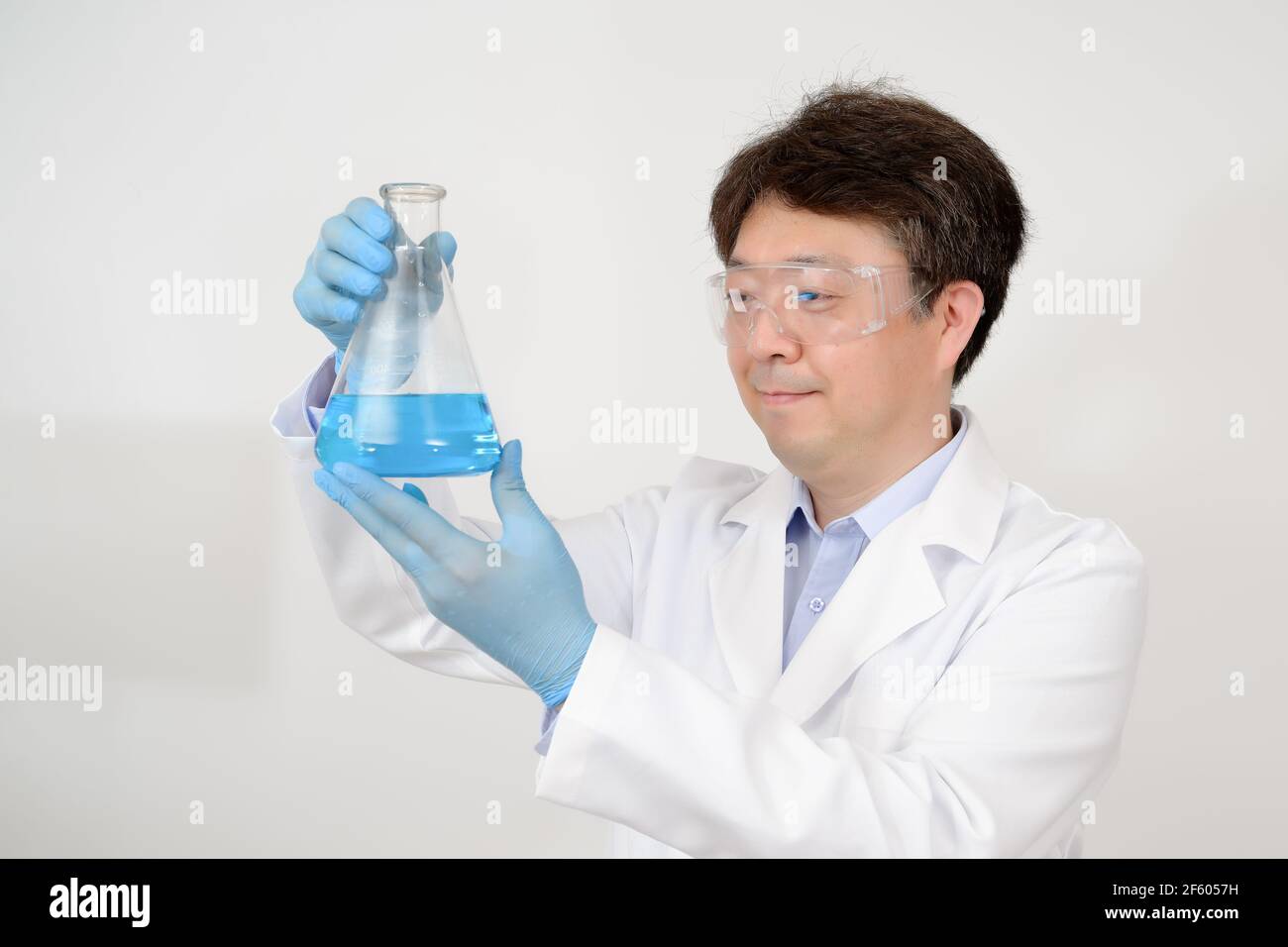 Portrait d'un scientifique asiatique de milieu d'année portant une blouse de laboratoire blanche et des gants et tenant un conteneur expérimental dans la main. Banque D'Images