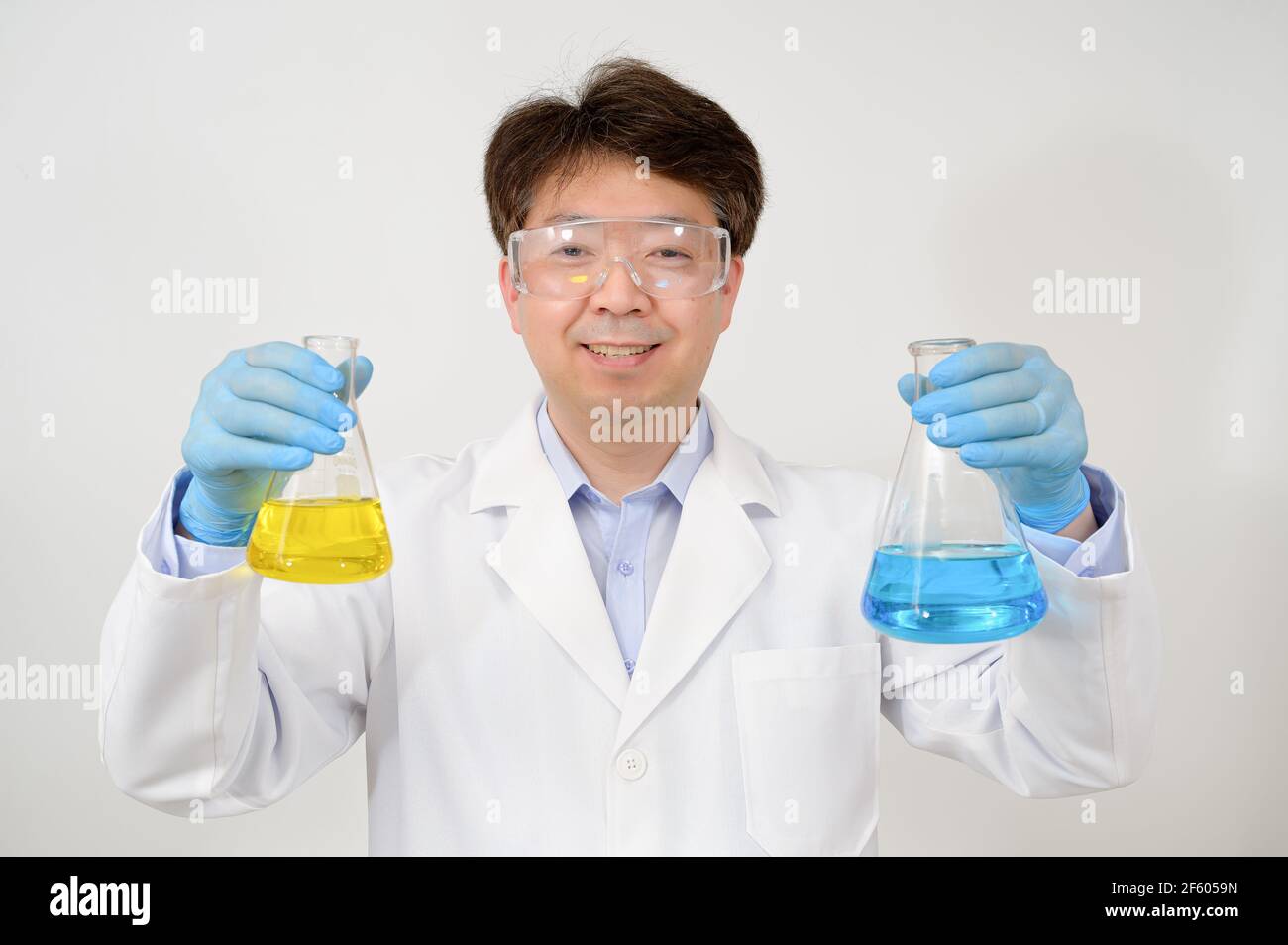 Portrait d'un scientifique asiatique de milieu d'année portant une blouse de laboratoire blanche et des gants et tenant un conteneur expérimental dans la main. Banque D'Images