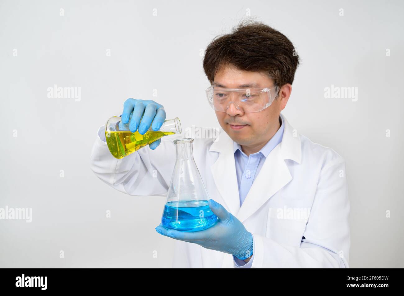 Portrait d'un scientifique asiatique de milieu d'année portant une blouse de laboratoire blanche et des gants et tenant un conteneur expérimental dans la main. Banque D'Images