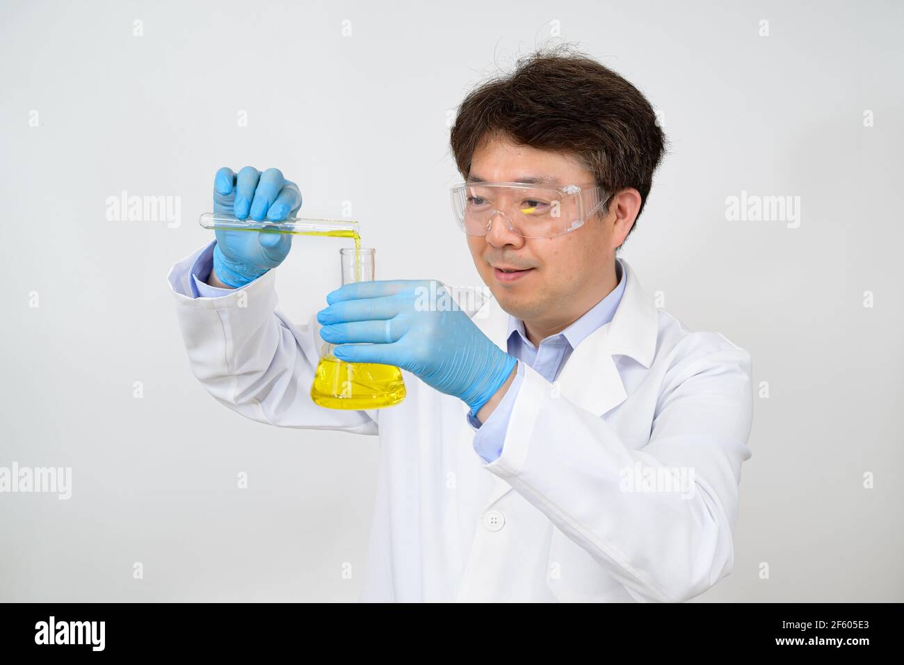 Portrait d'un scientifique asiatique de milieu d'année portant une blouse de laboratoire blanche et des gants et tenant un conteneur expérimental dans la main. Banque D'Images