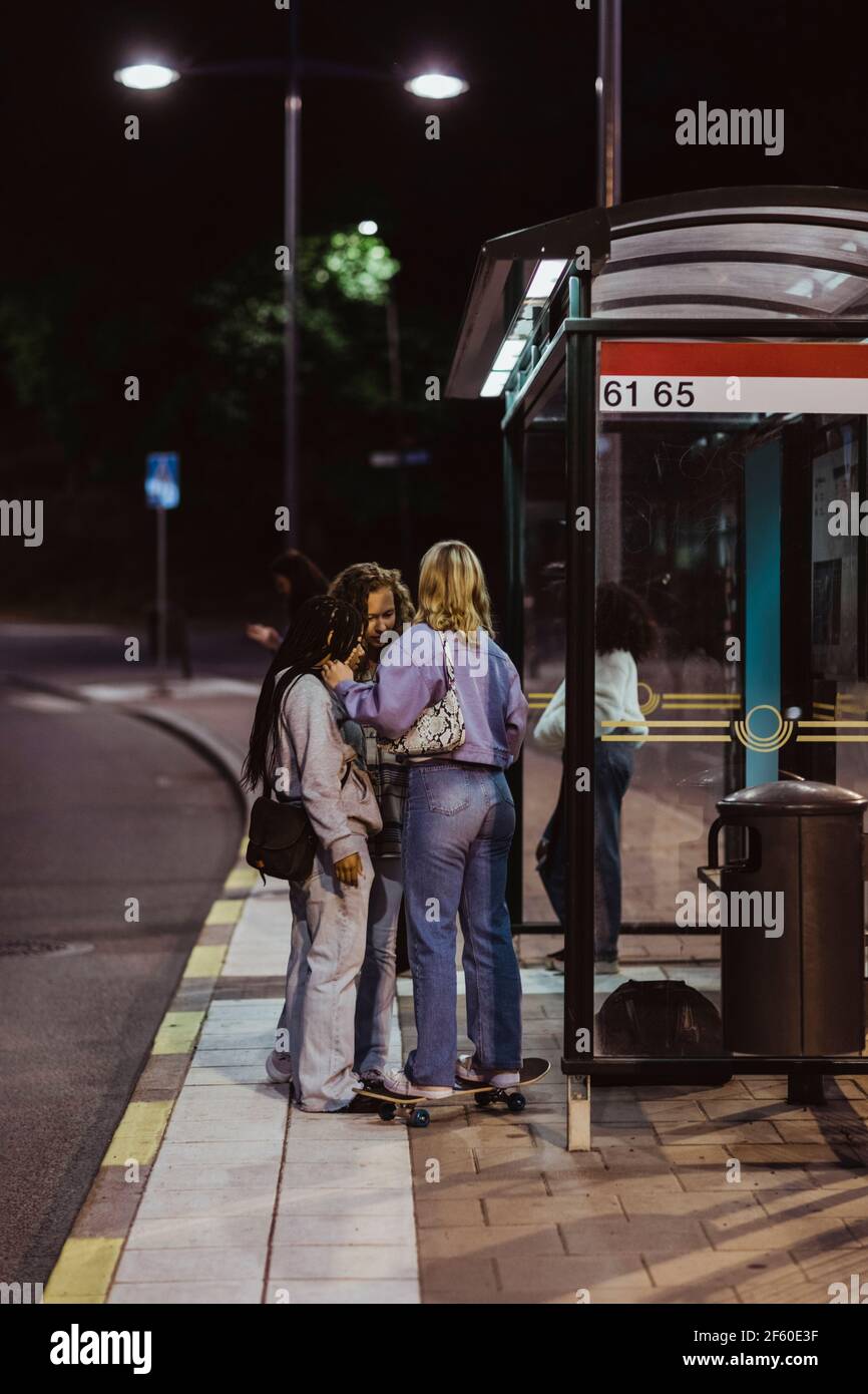 Des amies qui parlent en se tenant à l'arrêt de bus la nuit Banque D'Images