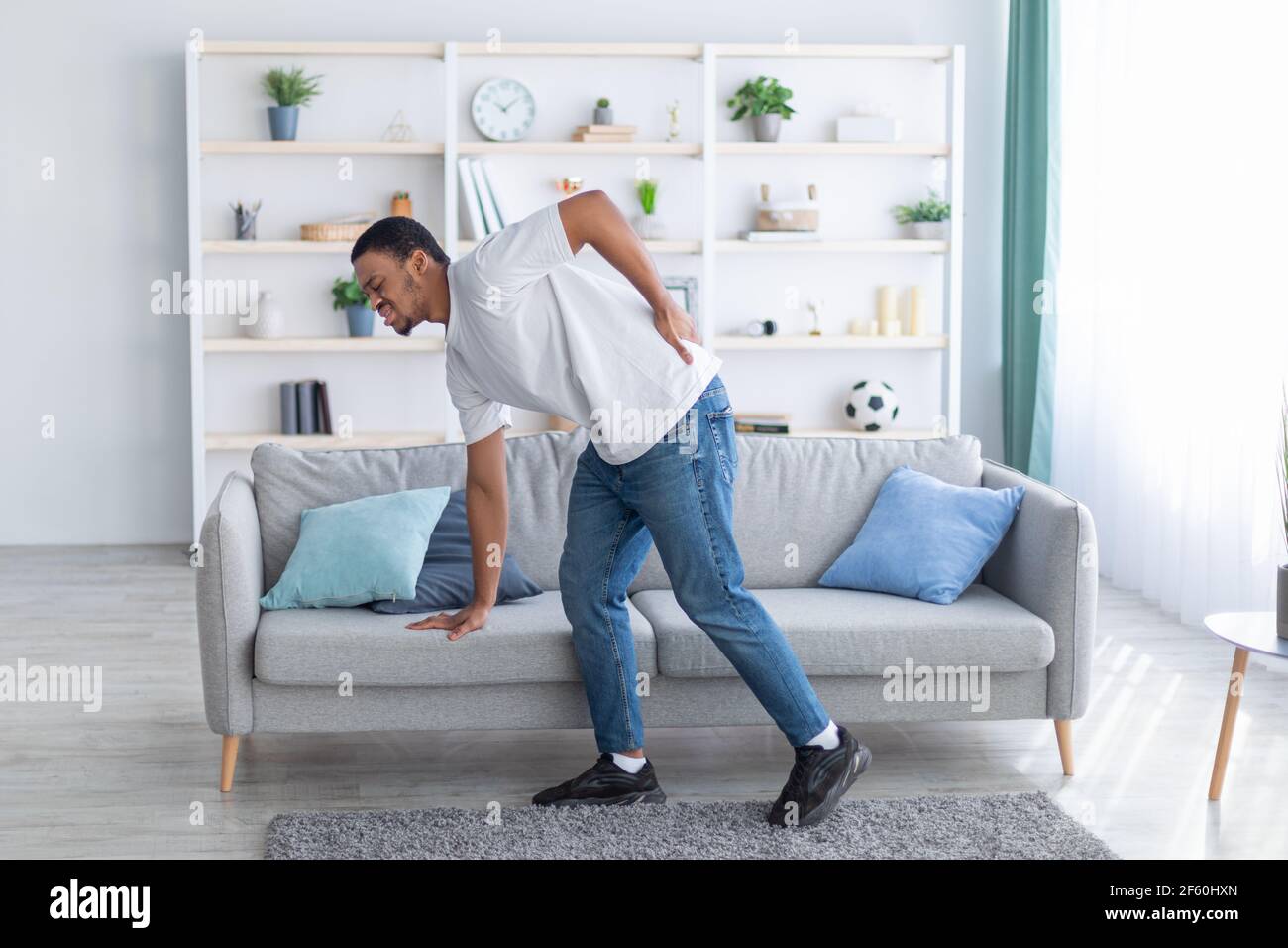 Un homme afro-américain millénaire souffrant de maux de dos, penché sur un canapé, ne peut pas marcher à la maison. Concept de soins de santé Banque D'Images
