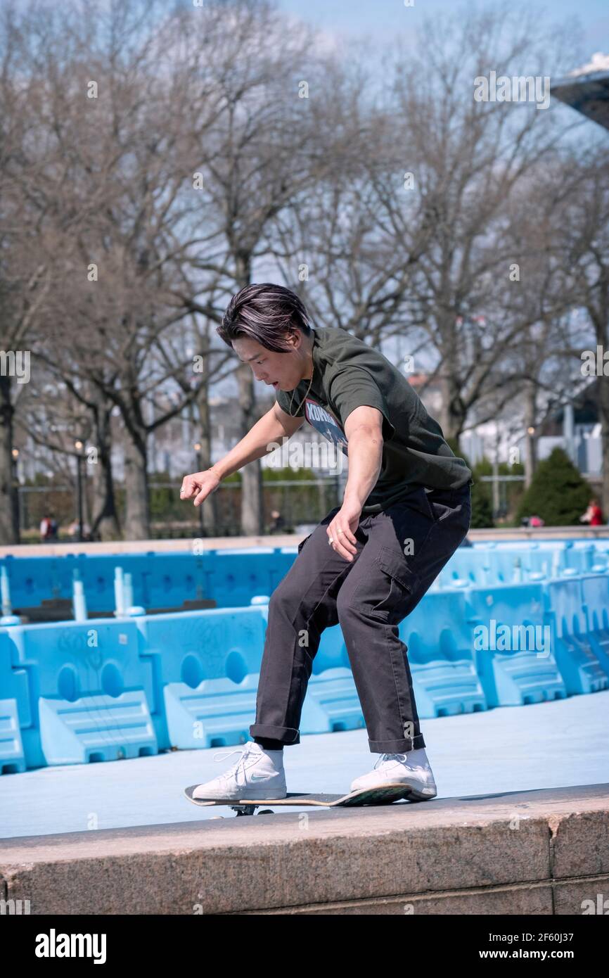 Un skateboarder américain d'Asie fait un tour de glisser sa planche le long d'un mince remblai de béton près de la Unisphere dans le parc de Flushing Meadows Corona. Banque D'Images