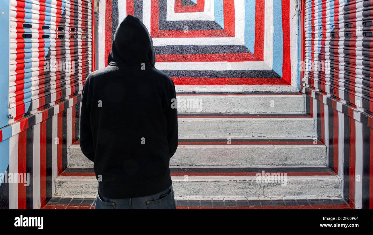 Silhouette de personne à capuche avec sweat-shirt à capuche gris et fond d'escalier avec des carrés rouges, blancs, noirs et bleus Banque D'Images