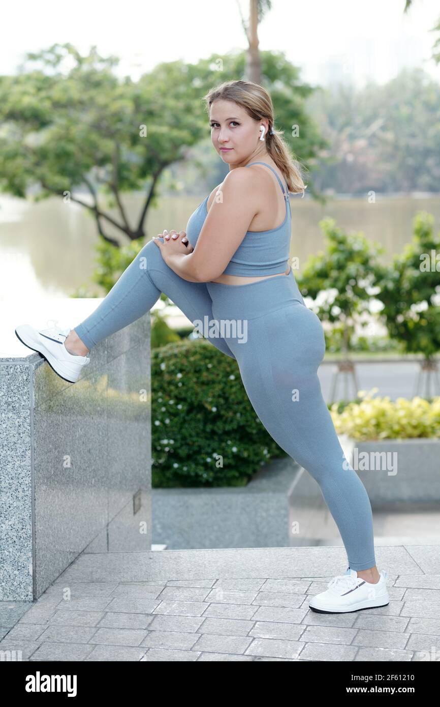 S'adapte aux jeunes femmes de taille plus en plaçant la jambe sur le mur de maintien pour vous détendre après l'entraînement et écouter de la musique dans les écouteurs Banque D'Images