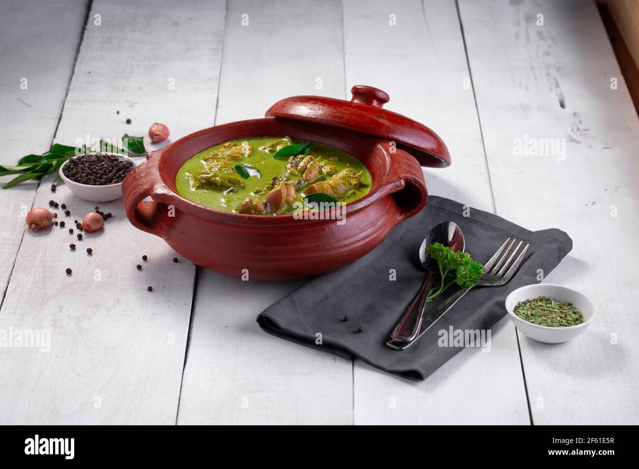 Curry de poulet vert avec ingrédients crus qui est disposé dans un matériel de terre avec fond blanc. Banque D'Images