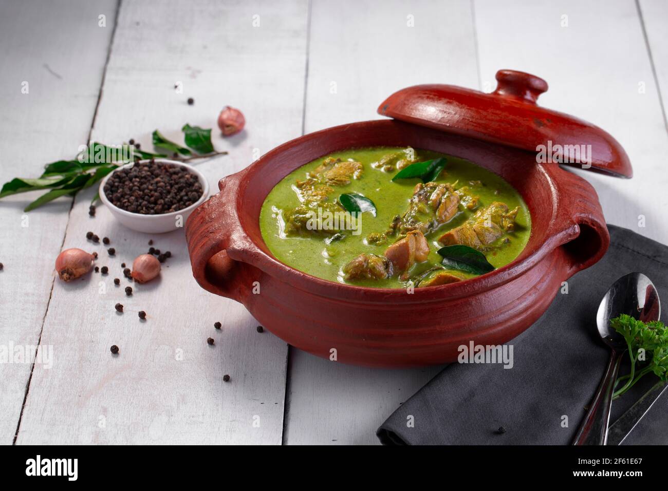 Curry de poulet vert avec ingrédients crus qui est disposé dans un matériel de terre avec fond blanc. Banque D'Images