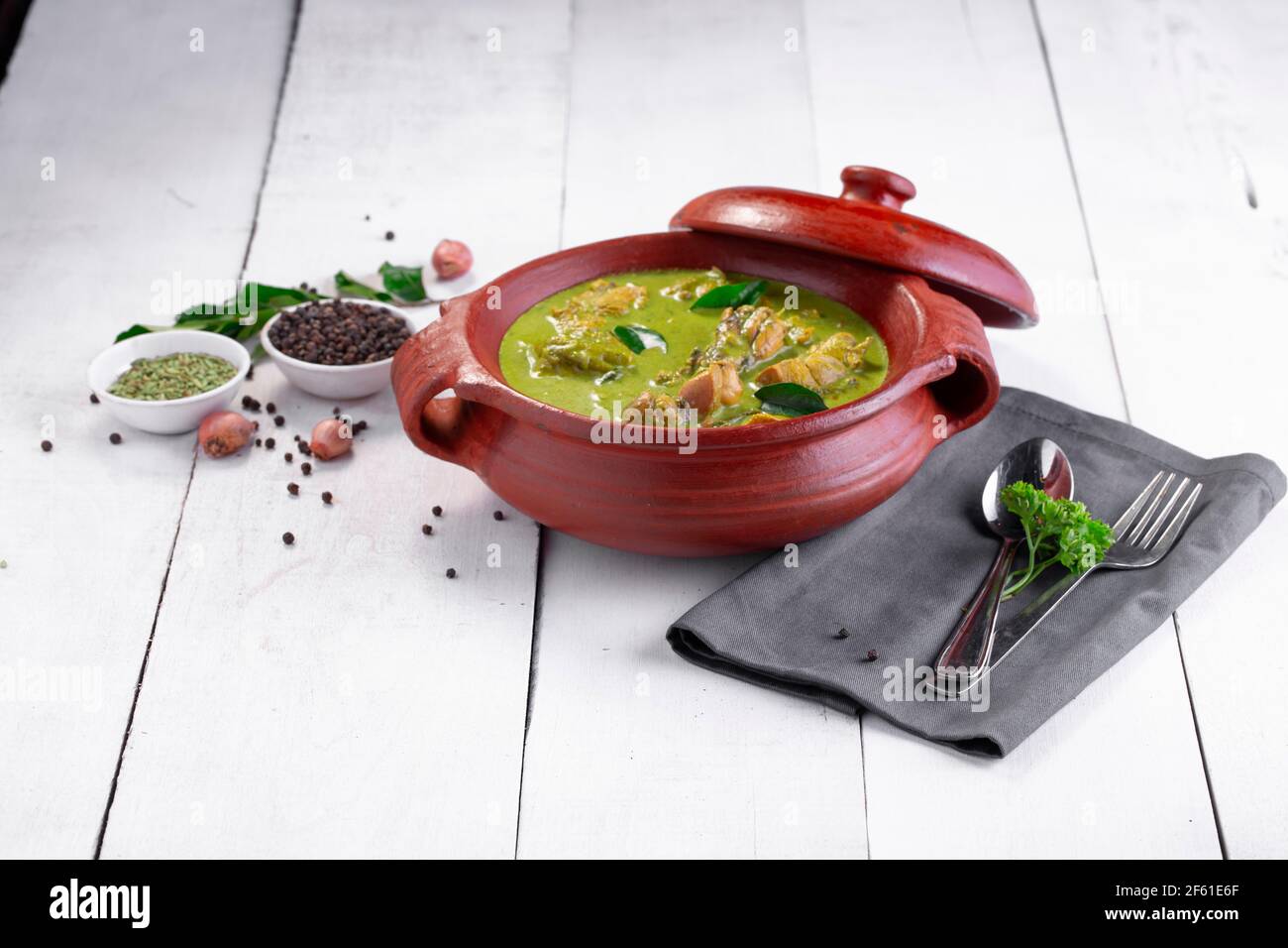 Curry de poulet vert avec ingrédients crus qui est disposé dans un matériel de terre avec fond blanc. Banque D'Images