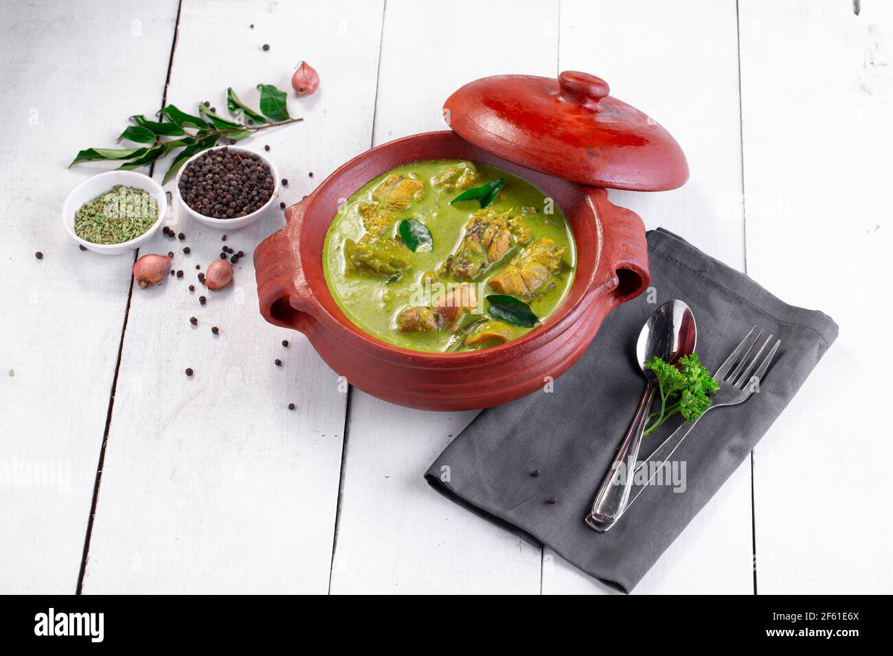 Curry de poulet vert avec ingrédients crus qui est disposé dans un matériel de terre avec fond blanc. Banque D'Images