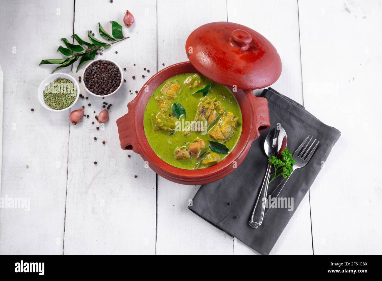 Curry de poulet vert avec ingrédients crus qui est disposé dans un matériel de terre avec fond blanc. Banque D'Images