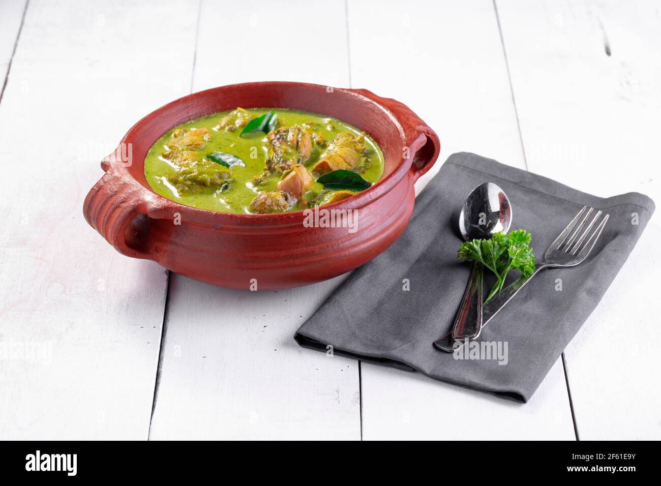 Curry de poulet vert avec ingrédients crus qui est disposé dans un matériel de terre avec fond blanc. Banque D'Images