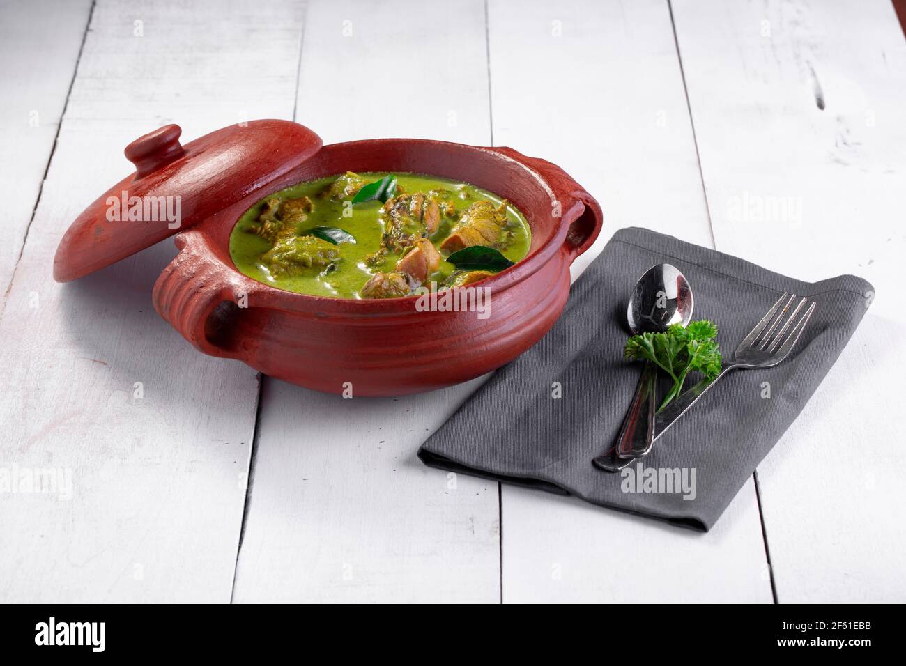 Curry de poulet vert avec ingrédients crus qui est disposé dans un matériel de terre avec fond blanc. Banque D'Images