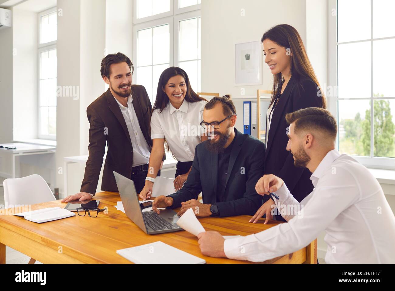 Les employés heureux de l'entreprise se réunissent au bureau et utilisent un ordinateur portable pour des recherches marketing ou des appels vidéo Banque D'Images