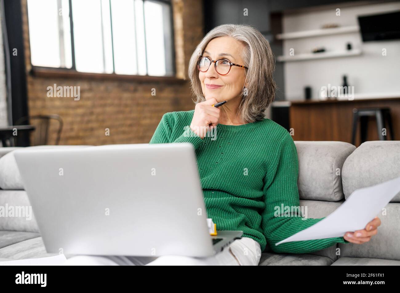 Femme séchée sur le canapé avec un ordinateur portable à la maison, elle tient du papier et prépare quelque chose, rêvant de passer des vacances Banque D'Images