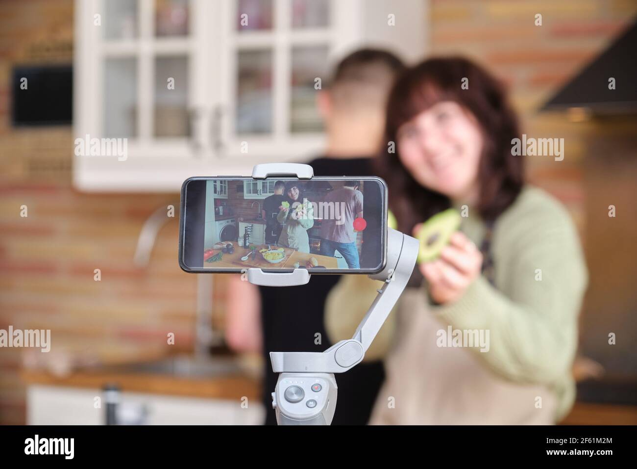 Jeune femme montrant un avocat à l'appareil photo et enregistrant une vidéo avec son smartphone pour sa chaîne de cuisine. Créateur de contenu et influenceur. Banque D'Images