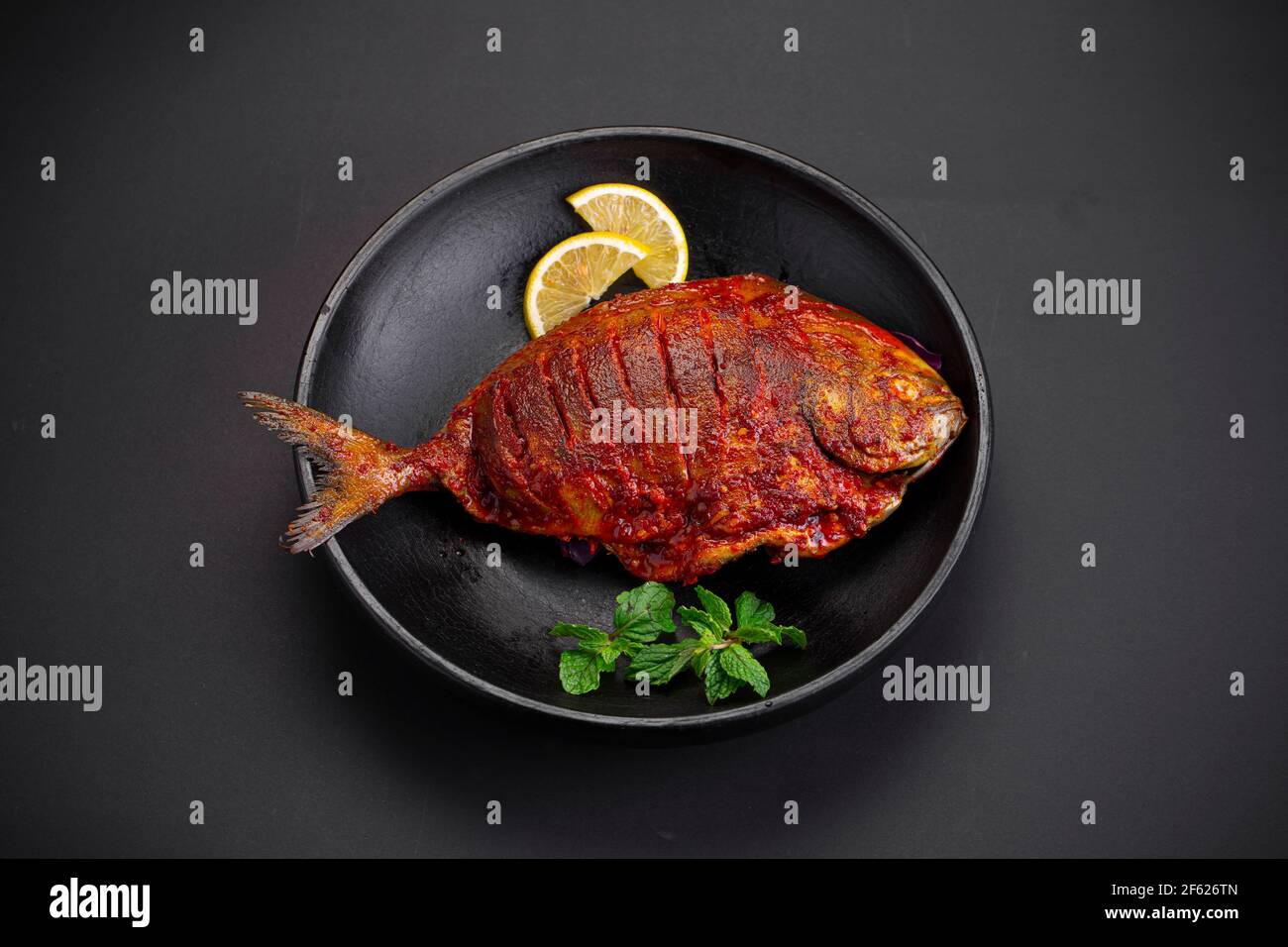 Frites au Pomfret disposées dans une assiette noire et garnies de tranches de citron sur fond noir texturé. Banque D'Images