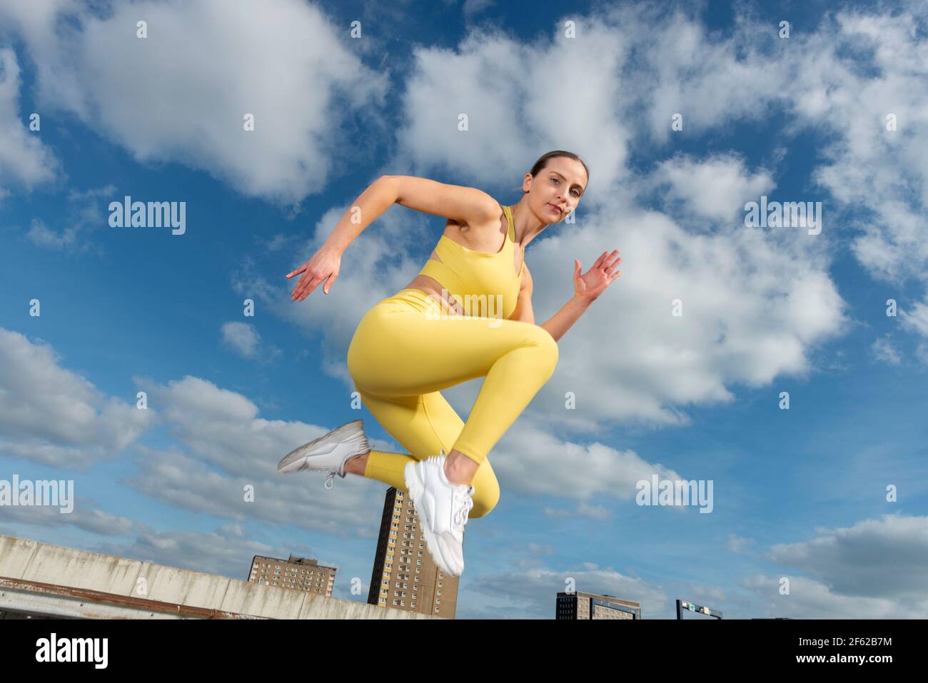 Femme sportive portant des vêtements d'activité jaunes en plein air, sautant pendant la course. Banque D'Images