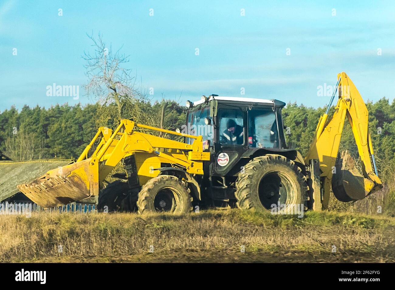 Biélorussie, région de Minsk - 19 décembre 2019 : bulldozer dans un champ de campagne sur fond de forêt ensoleillée. Banque D'Images