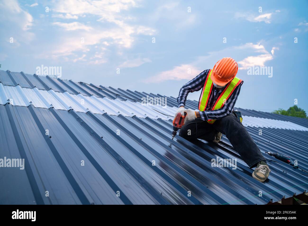 Asian Roofer Worker porter des vêtements de sécurité à l'aide d'un pistolet pneumatique ou pneumatique et installer sur une nouvelle tôle de toit, concept de toit de bâtiment résidentiel sous con Banque D'Images