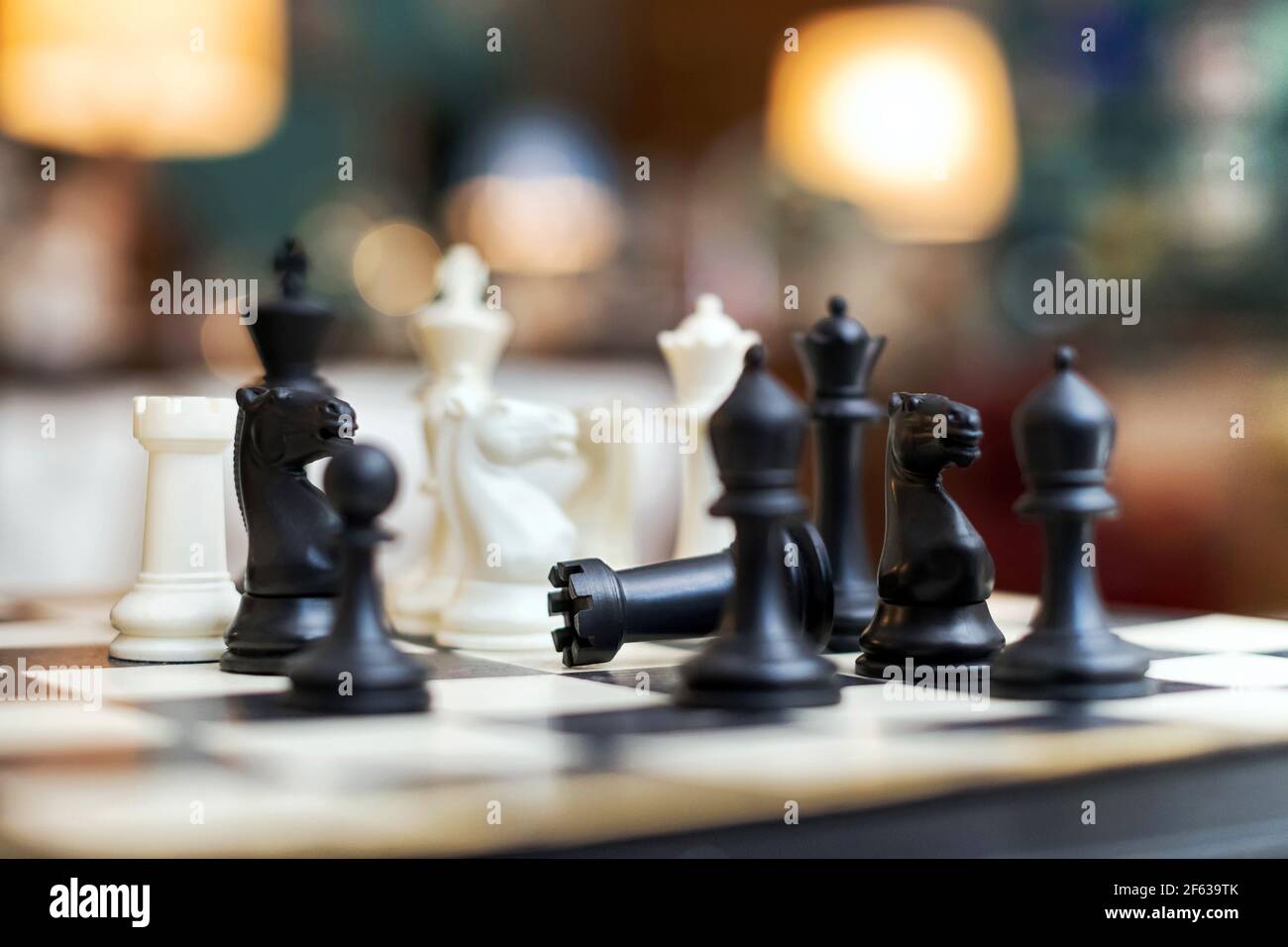 Vue rapprochée à angle bas d'un et noir en bois jeu d'échecs blanc sur un échiquier avec un foyer sélectif à un château tombé au centre des pièces dans a Banque D'Images