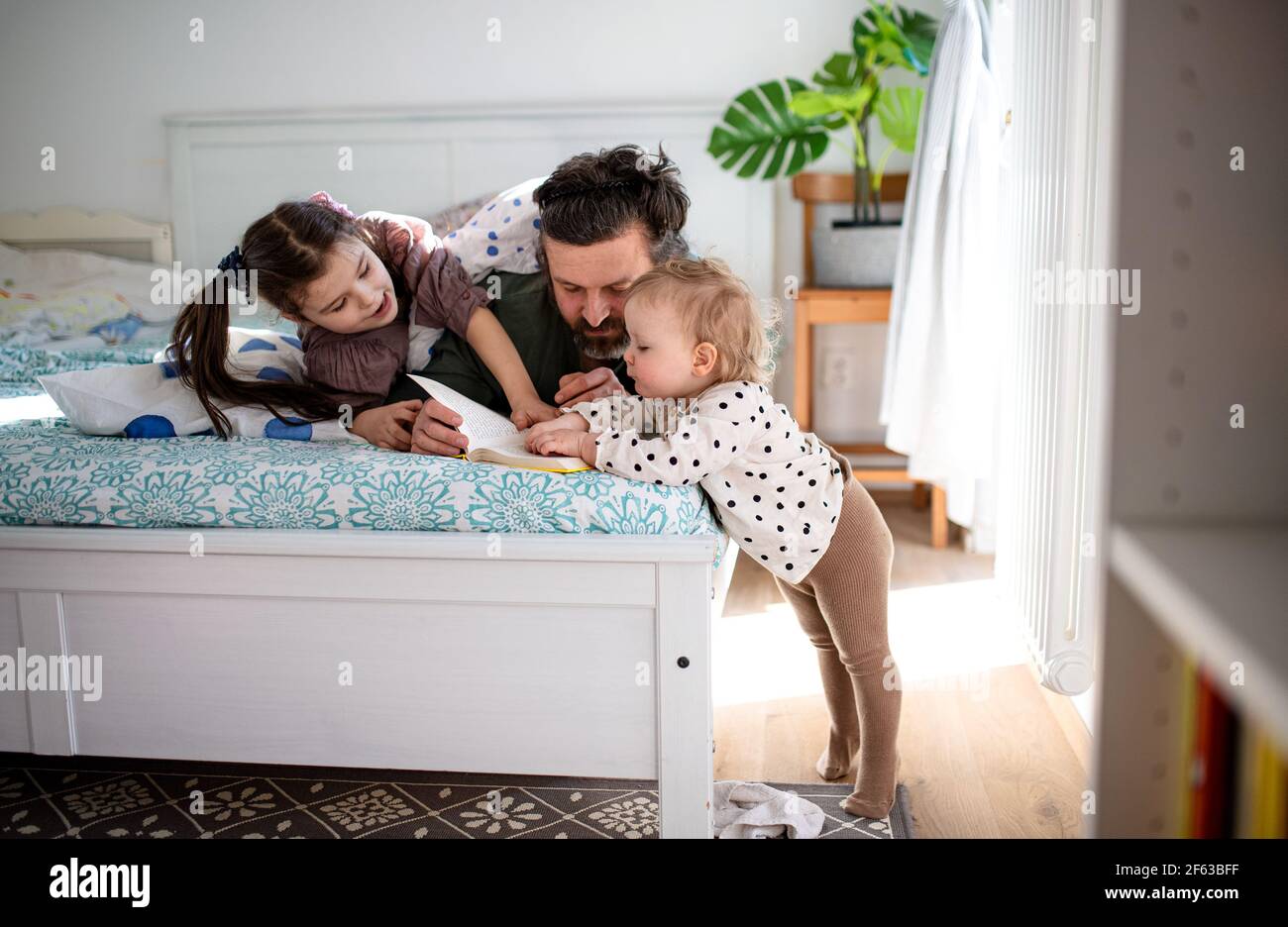 Père avec deux petites filles s'amusant sur le lit à la maison. Banque D'Images