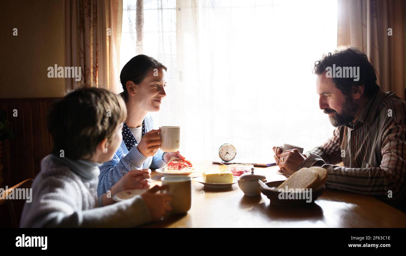 Portrait d'une petite fille triste pauvre avec des parents mangeant à l'intérieur à la maison, concept de pauvreté. Banque D'Images