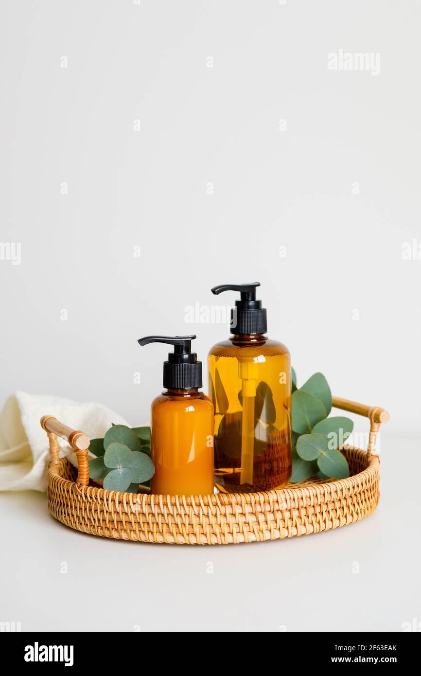 Plateau en rotin avec bouteilles de shampooing ou gel douche en verre ambré, branches d'eucalyptus, serviette. SPA de cosmétiques biologiques naturels sur la table de bain Banque D'Images