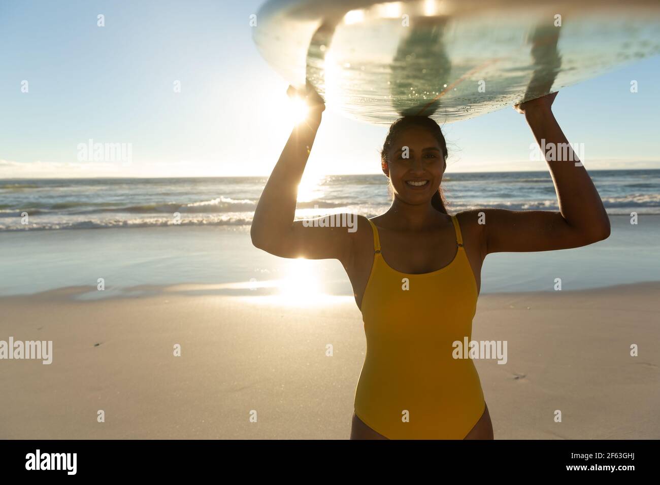 Bonne femme de course mixte sur la plage portant la planche de surf tête Banque D'Images