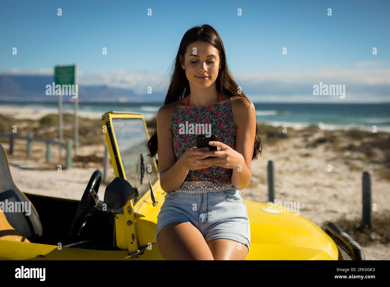 Bonne femme caucasienne assise sur une promenade de plage au bord de la mer à l'aide d'un smartphone Banque D'Images