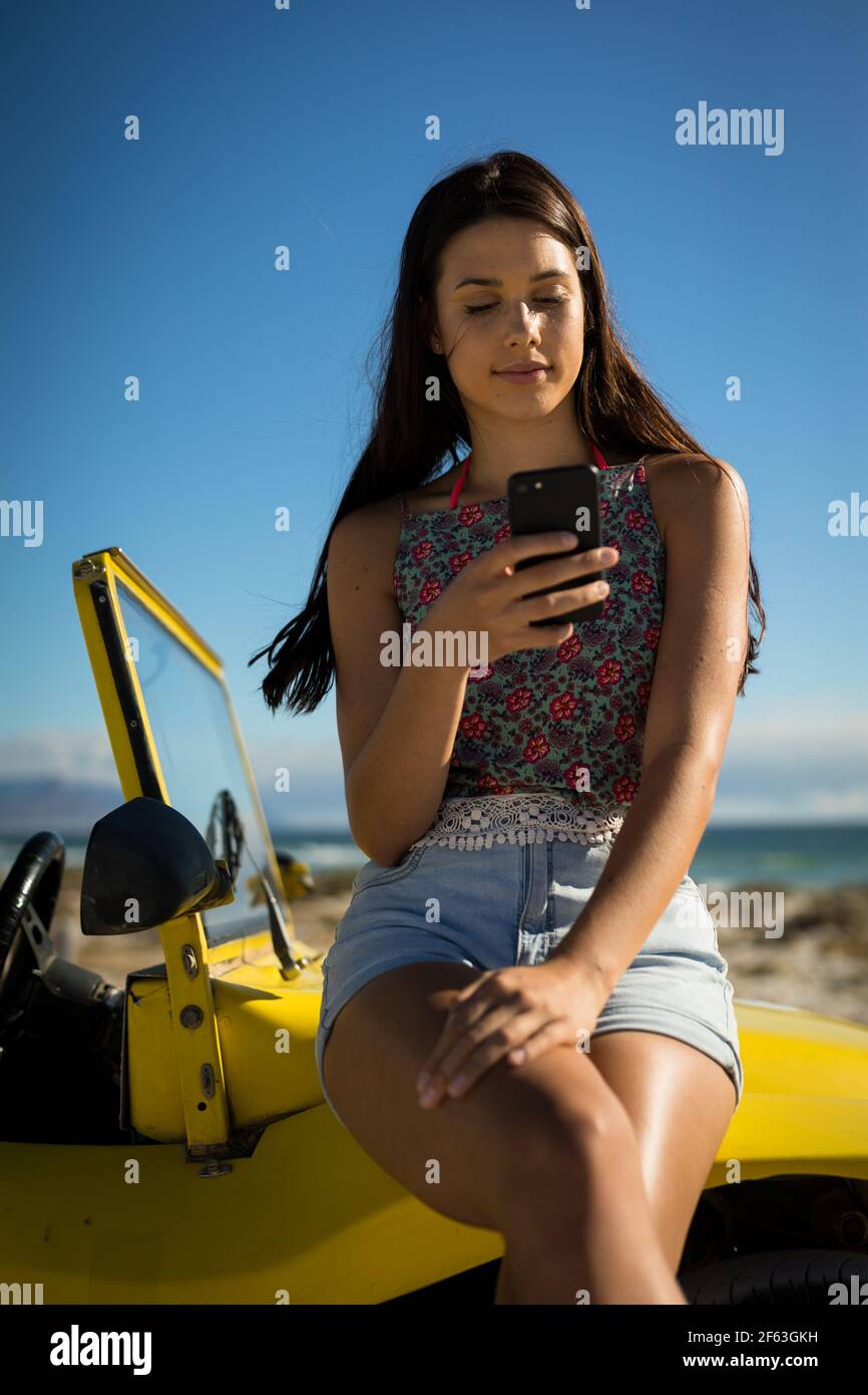 Bonne femme caucasienne assise sur une promenade de plage au bord de la mer à l'aide d'un smartphone Banque D'Images