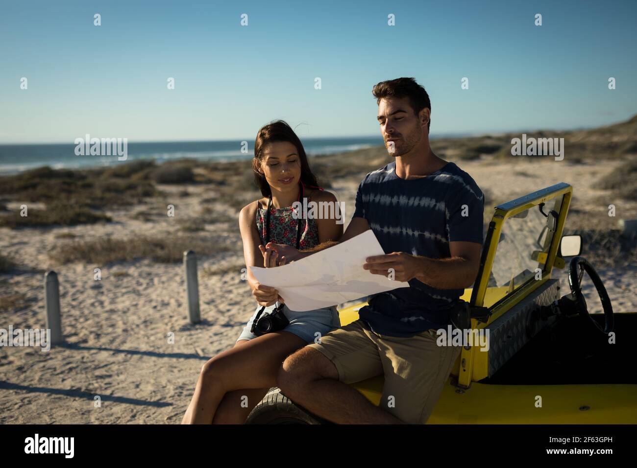 Heureux couple caucasien assis sur la plage buggy au bord de la mer lecture de la feuille de route Banque D'Images