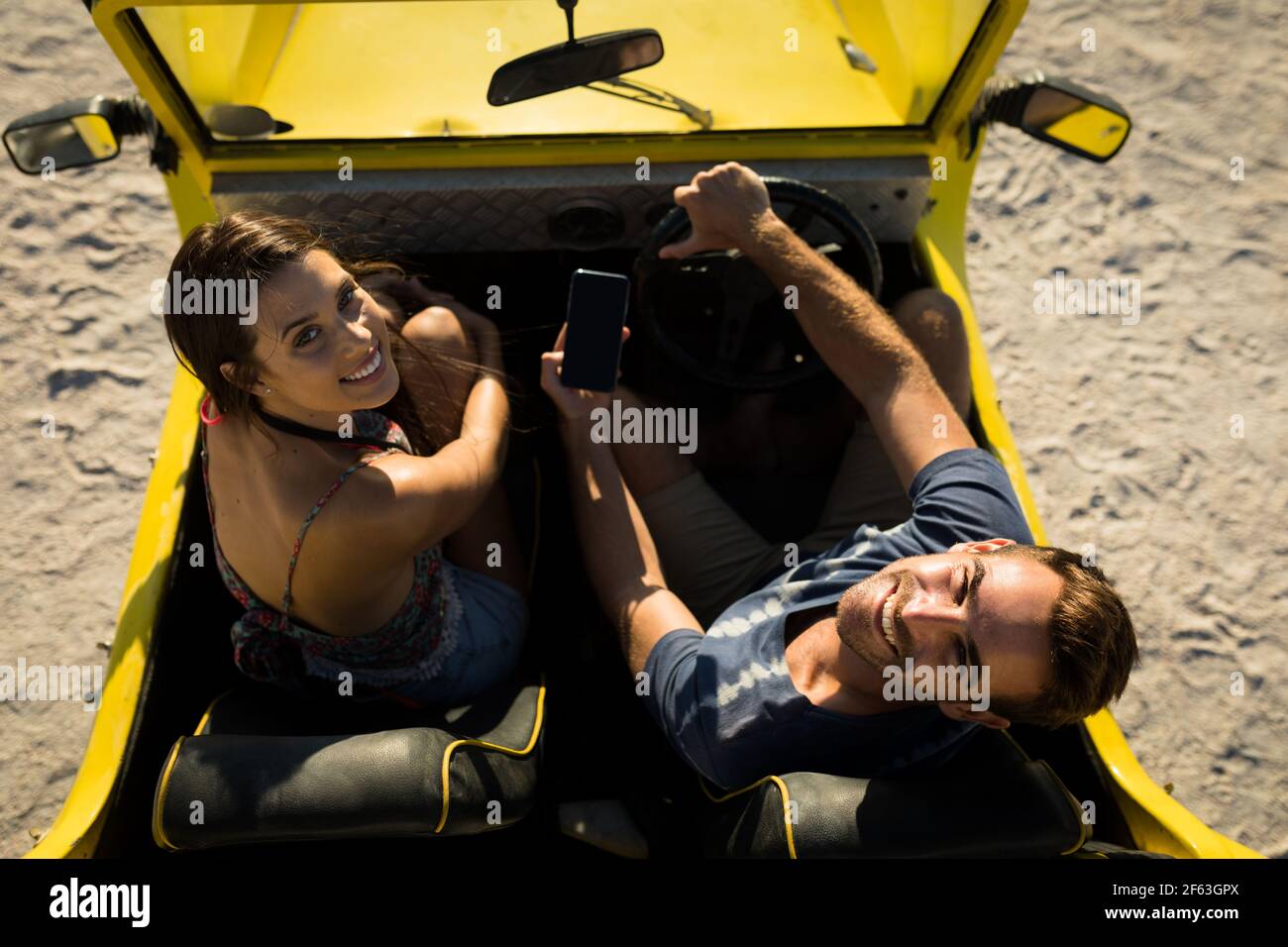 Heureux couple caucasien assis dans la plage buggy au bord de la mer à l'aide d'un smartphone Banque D'Images