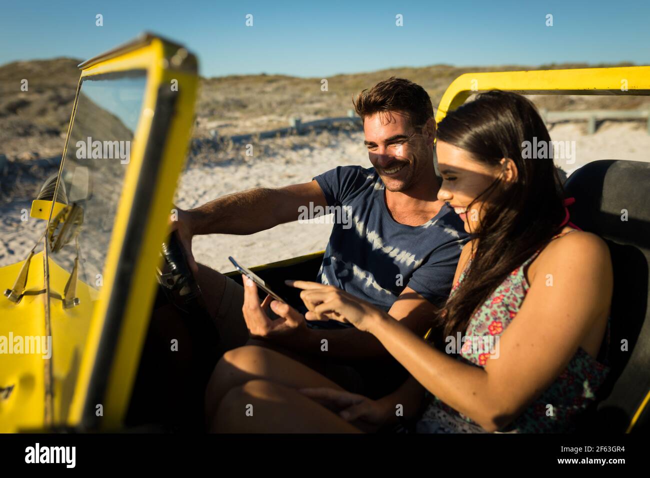 Heureux couple caucasien assis dans la plage buggy au bord de la mer à l'aide d'un smartphone Banque D'Images