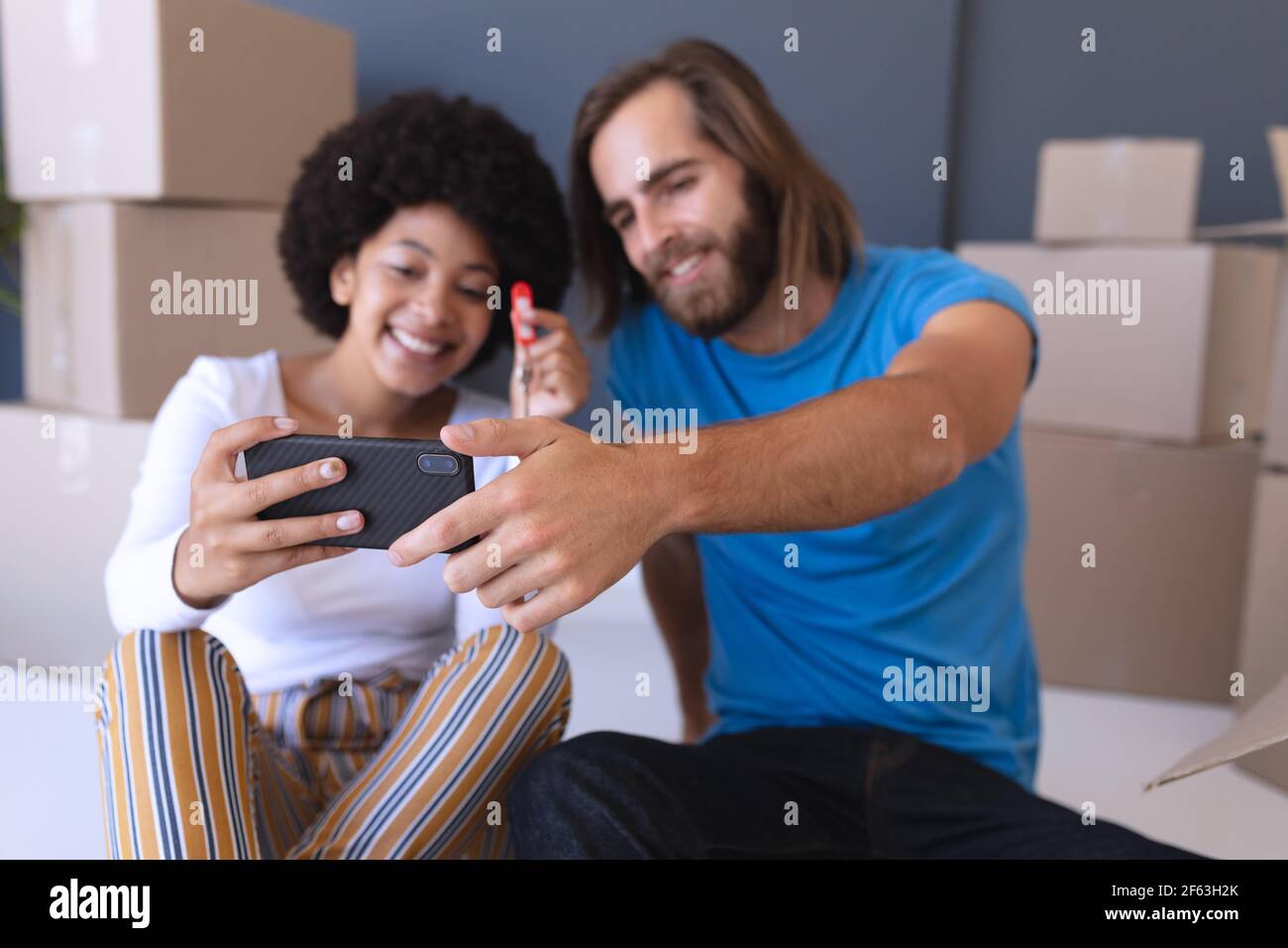 Heureux couple divers déménagent assis à la maison et utilisant le smartphone Banque D'Images