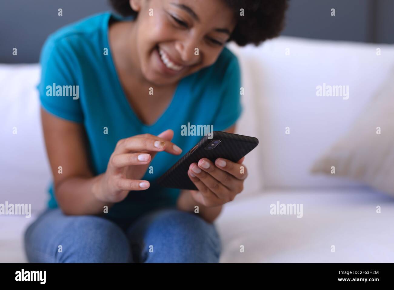 Femme afro-américaine assise sur un canapé à l'aide d'un smartphone Banque D'Images
