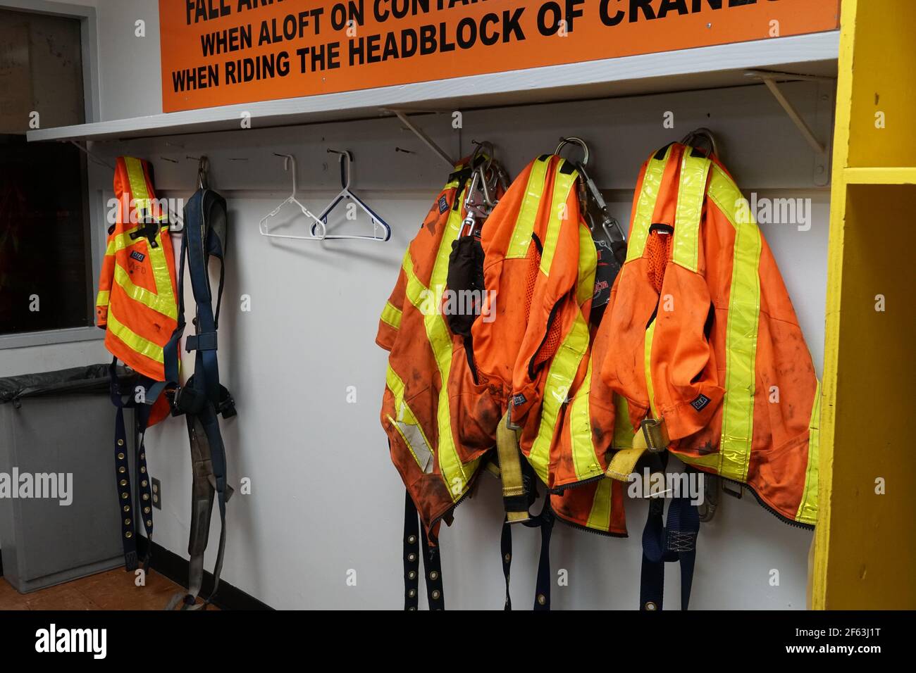 Équipement antichute et gilets de sécurité orange à haute visibilité suspendus dans la salle d'opération pour les articles de stevedores utilisés lorsqu'ils sont en bon état de marche pendant l'arrimage. Banque D'Images