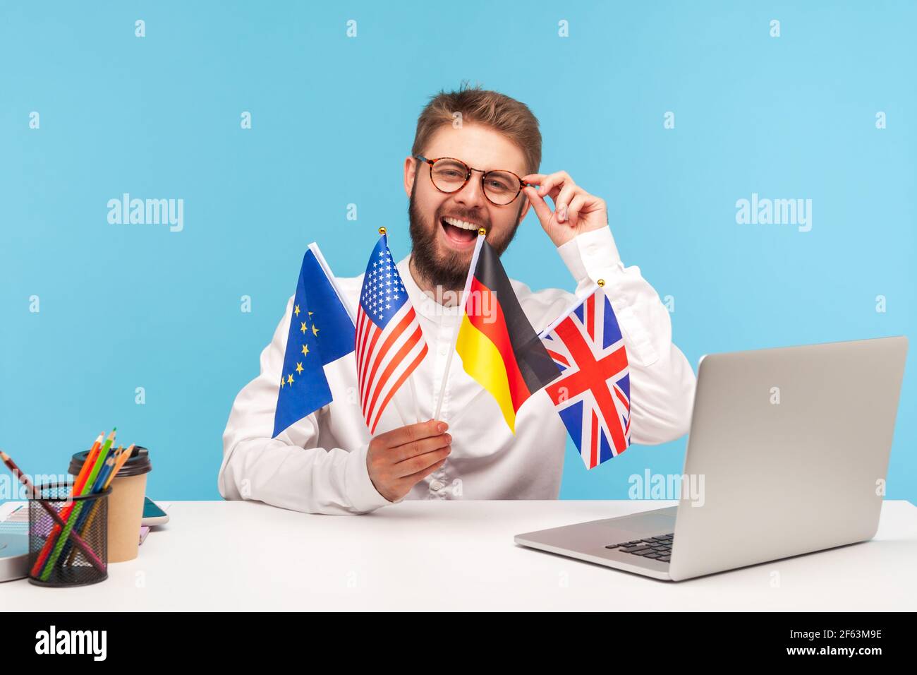 Homme souriant enseignant ajuster des lunettes tenant des drapeaux des etats-unis, de l'allemagne, de la Grande-bretagne et de l'europe pays, la publicité des langues étrangères étudiant scho Banque D'Images