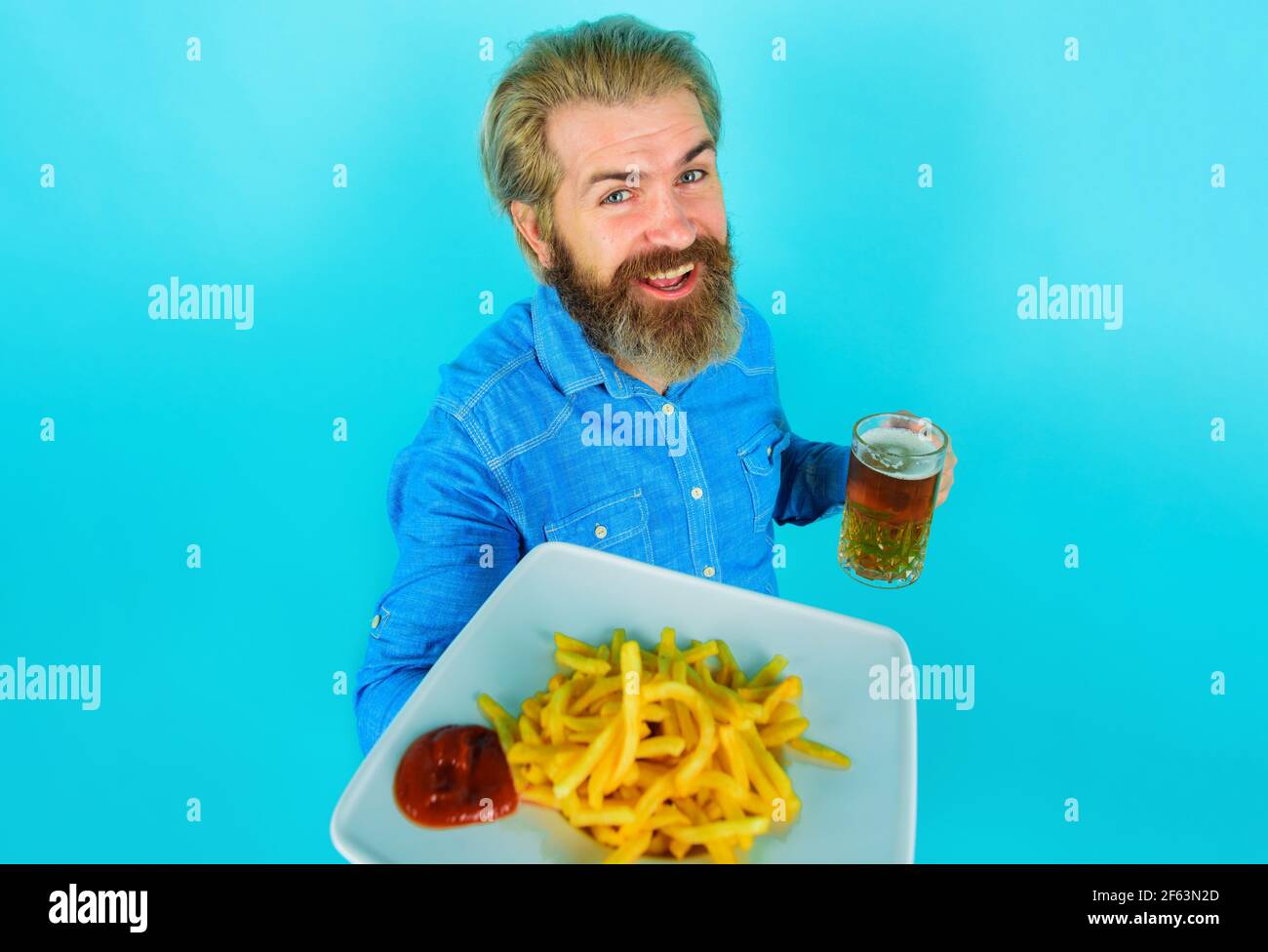 Homme souriant avec des pommes de terre frites et de la bière. Pommes de terre frites. Mâle barbu avec pommes de terre frites et ketchup sur l'assiette. Banque D'Images