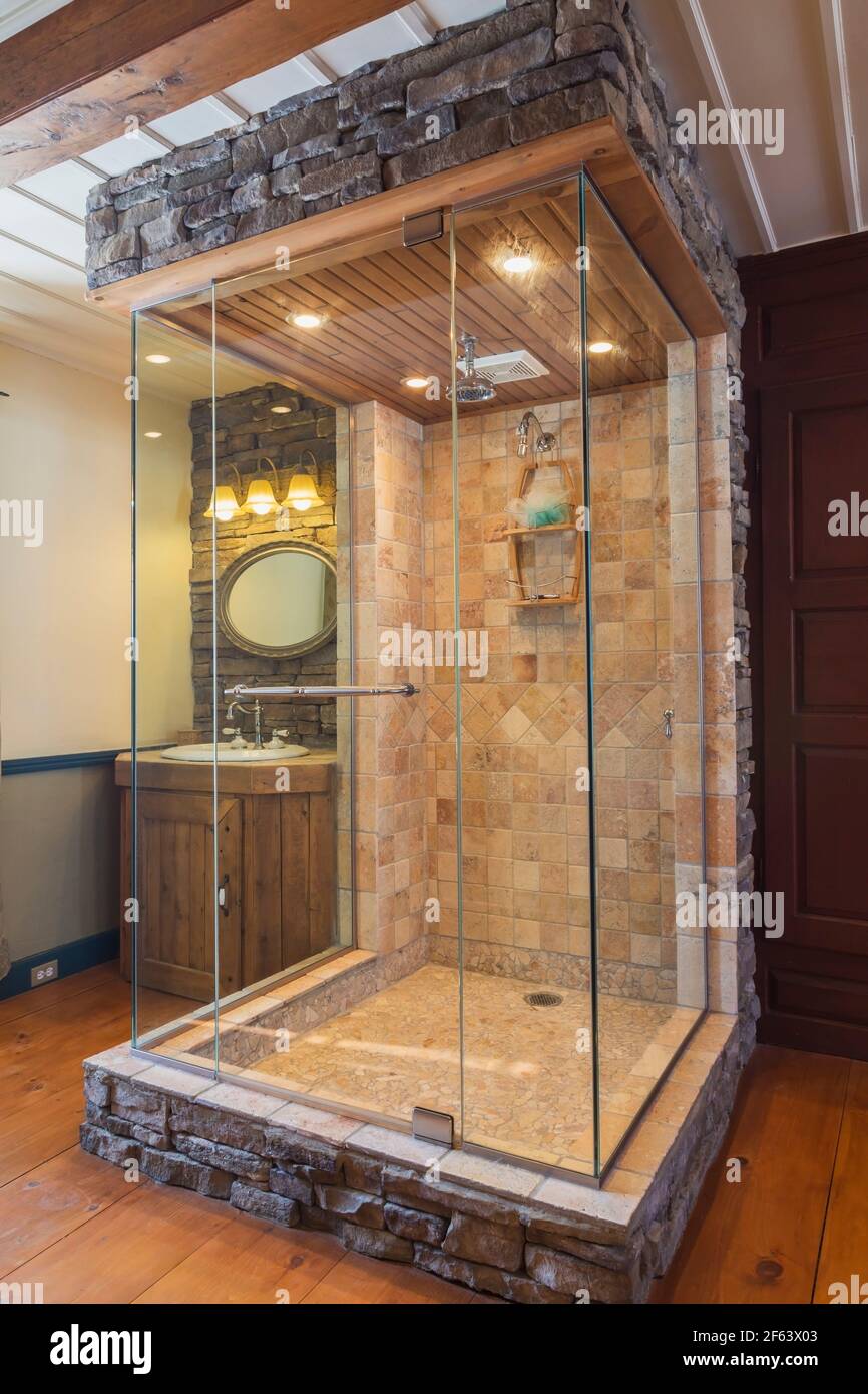Cabine de douche beige et beige en céramique et pierre coupée avec panneaux en verre transparent à trois côtés, plafond en bois de cèdre et meuble-lavabo dans la salle de bains ouverte Banque D'Images