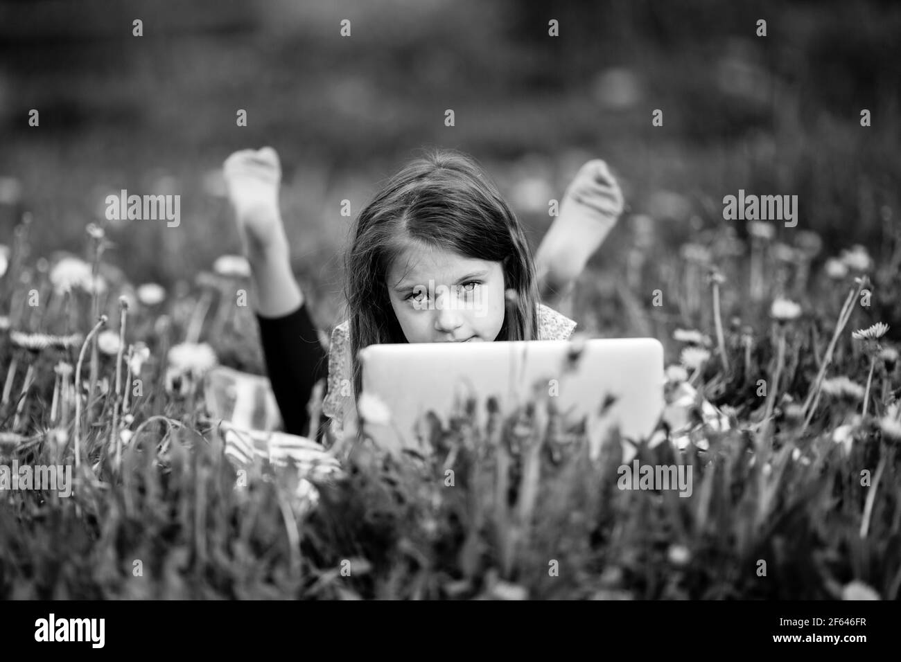 Petite fille avec un ordinateur portable couché à l'extérieur en été. Photo en noir et blanc. Banque D'Images